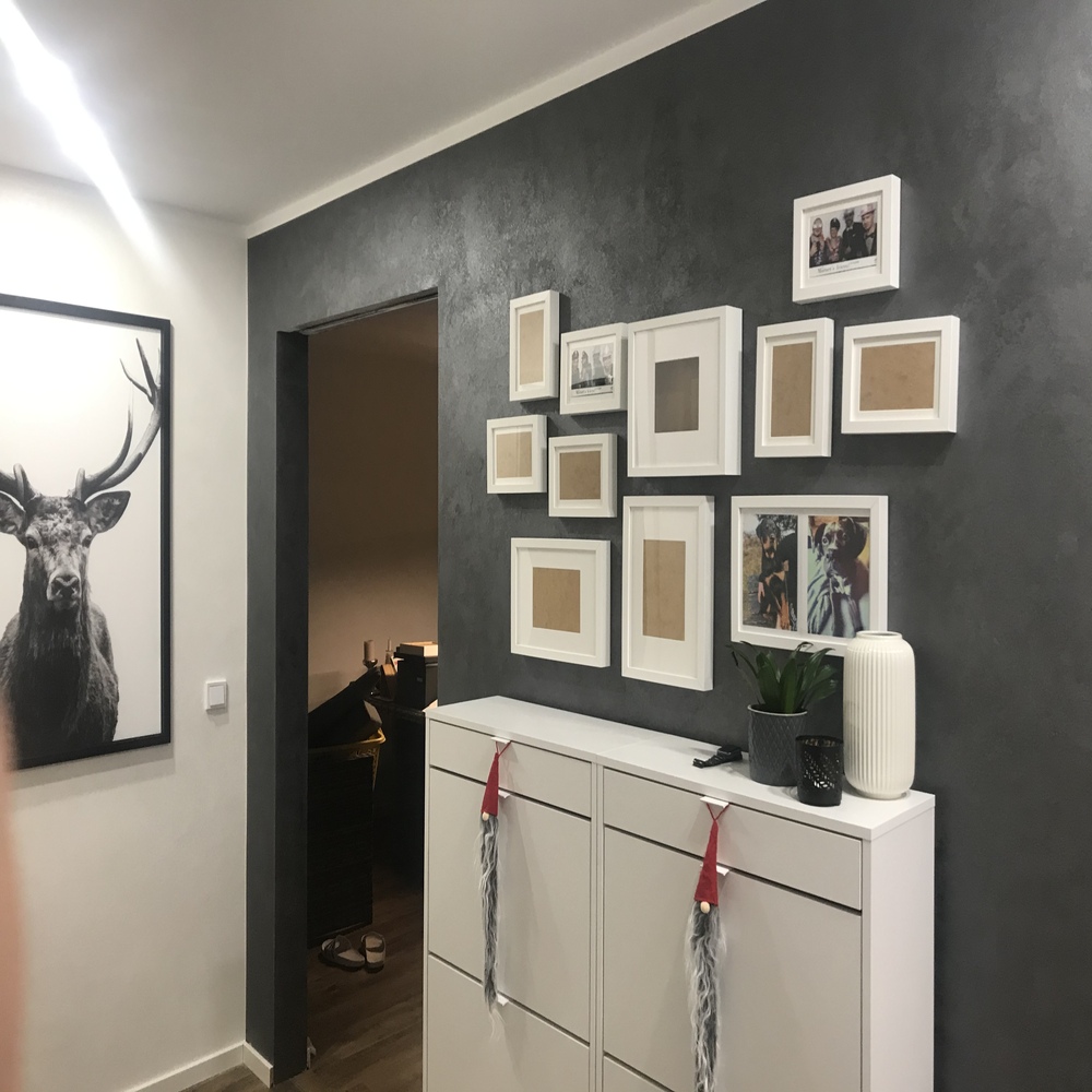 Wanddekoration mit schwarz-weißem Druck einer klassischen Statue und sichtbaren Buchstaben neben einer modernen schwarzen Treppe.